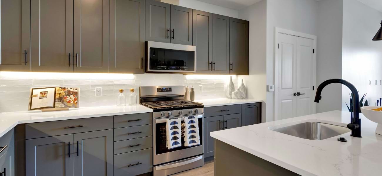 Modern kitchen with sleek grey cabinets, stainless steel appliances, and elegant white countertops, featuring a stylish island sink. Modern kitchen with sleek grey cabinets, stainless steel appliances, and elegant white countertops, featuring a stylish island sink.