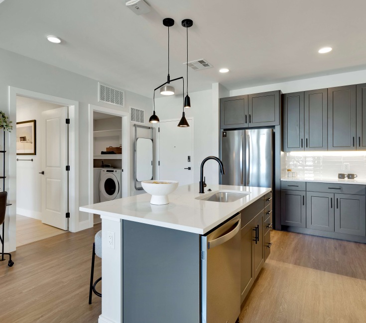 Modern kitchen with sleek dark cabinets, elegant pendant lighting, and a spacious island with integrated sink, offering a stylish workspace.	