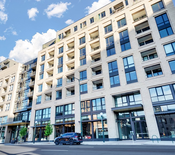 Modern apartment building exterior with sleek glass windows, inviting balconies, and stylish entrance in a sunny urban setting.	